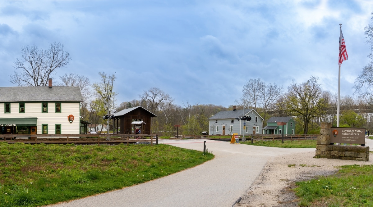 A photograph depicting the Boston Mill Visitor Center in Cuyahoga Valley National Park. The image includes a National Park sign and the former Cleveland-Akron Bag Company general store.