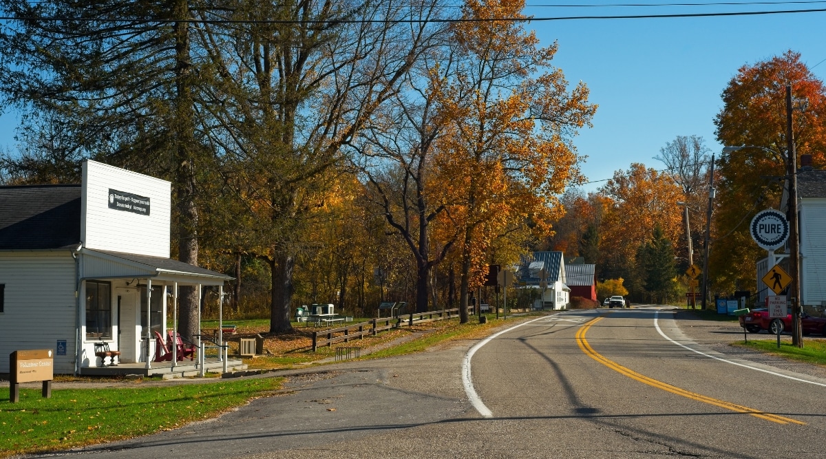 A street-level view capturing Boston Township in Ohio. The image showcases a typical roadway, with a car driving down the road. The trees lining the street display yellow-orange leaves, indicative of autumn foliage. 
