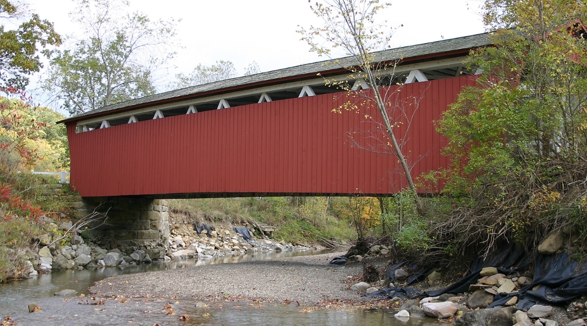 Everett covered bridge in Ohio built in the 18th century. The bridge is dark red and functions over the river. It is old and historic.