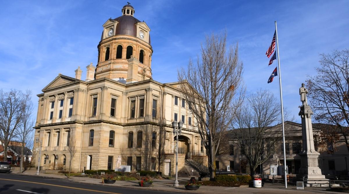 The Tuscarawas County Courthouse in New Philadelphia, Ohio is a Neoclassical-style government building, featuring a white limestone facade, a dome with a clock tower, a grand entrance with fluted columns, and a pediment.