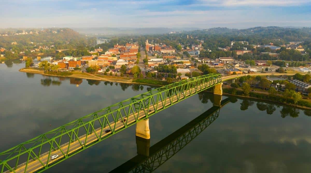 The Muskingum River in Marietta, Ohio is a historic waterway that runs through the city and offers scenic views of the surrounding hills and low-rise valleys. There are also two bridges across the river, one of which is green and the other is brown.