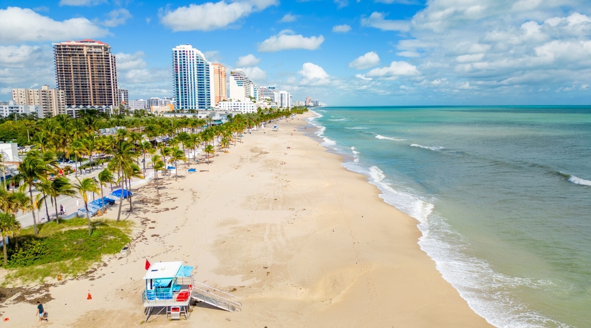 Fort Lauderdale Beach is a popular tourist destination in Florida with crystal clear waters and soft, sandy beaches. Top view of a beautiful beach and promenade with bars, cafes, shops, hotels and tall palm trees.