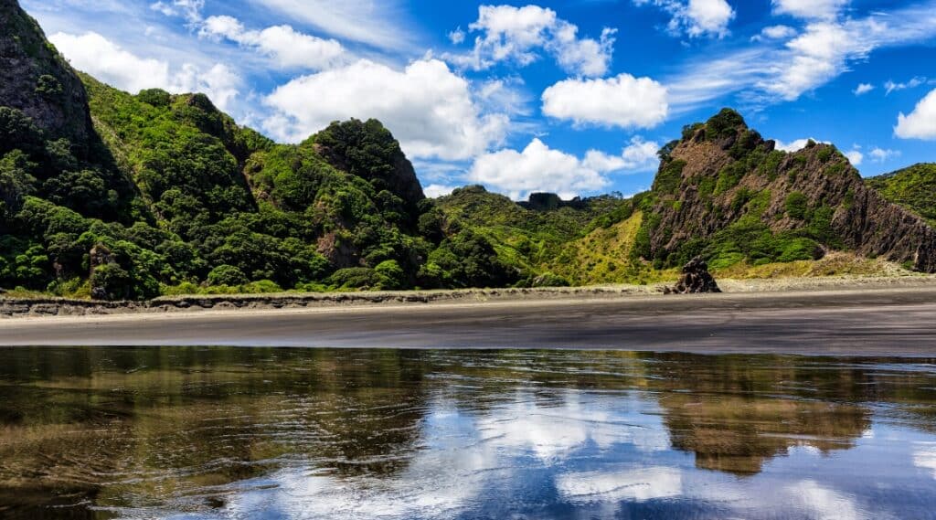 Karekare Beach is a stunning black sand beach located in Auckland, New Zealand. The beach is surrounded by lush greenery, rocks and waterfalls.