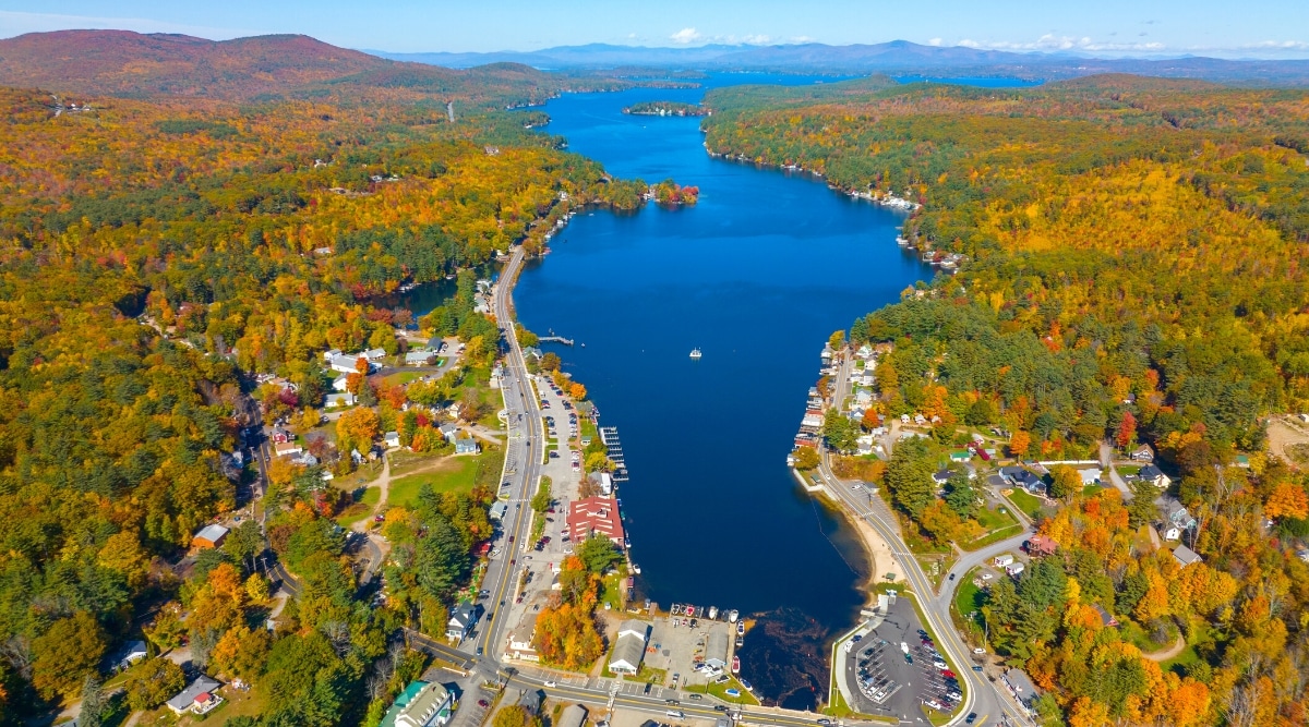 Lake Winnipesaukee is a large freshwater lake in the Lakes Region of New Hampshire. Top view of a blue lake surrounded by towns and autumn forests.