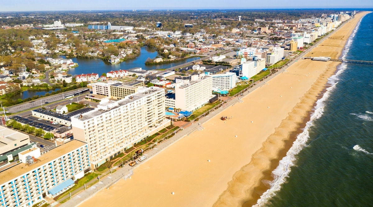 Ocean City Beach in Maryland is a popular destination known for its long stretch of clean, sandy beach, bustling boardwalk with amusement parks, restaurants, and shops. Top view of blue ocean, golden beach surrounded by hotels, buildings, shops and restaurants.