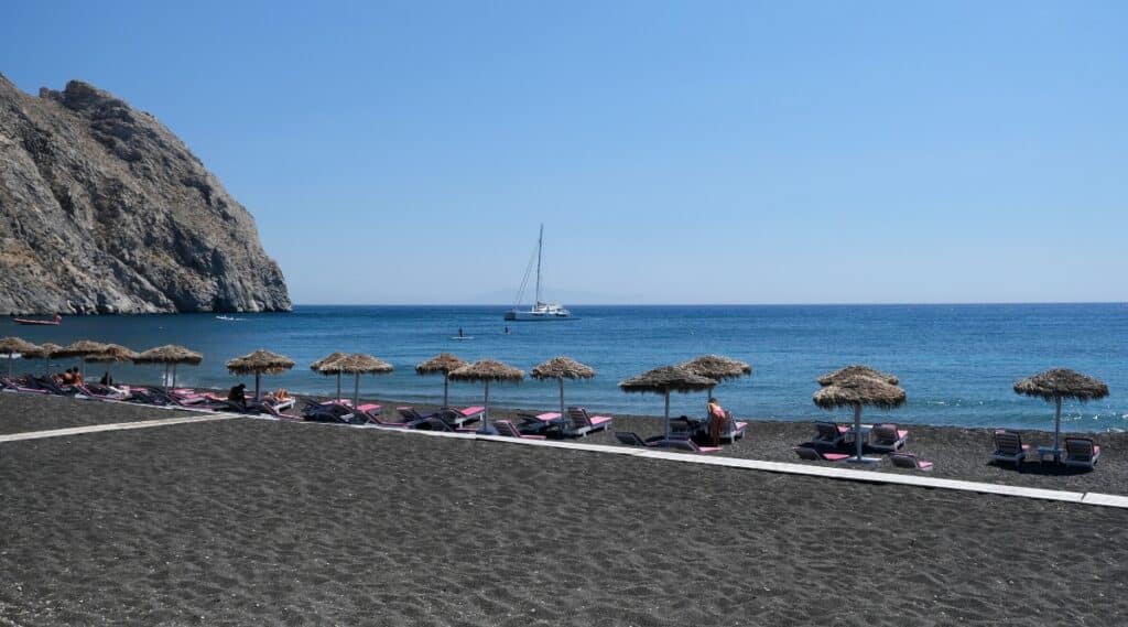 Perissa Beach is a black sand beach located on the southeast popular coast of Santorini, Greece. The beach is known for its clear blue water, black sand and beautiful scenery surrounded by steep cliffs. The beach is equipped with sun loungers and straw umbrellas.