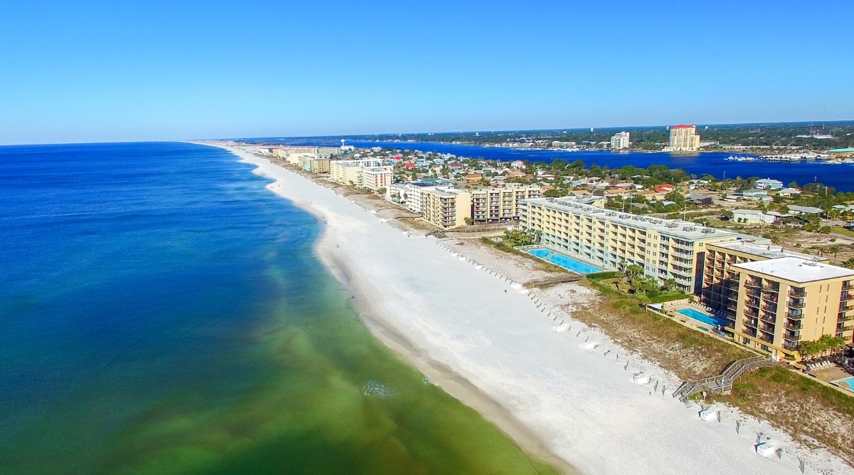 The South Walton Beaches in Florida are a collection of 16 beach neighborhoods that span 26 miles along the Gulf of Mexico. top view of a long beach with sugar white sand and clear emerald green water. The beach has many hotels, restaurants and shops.