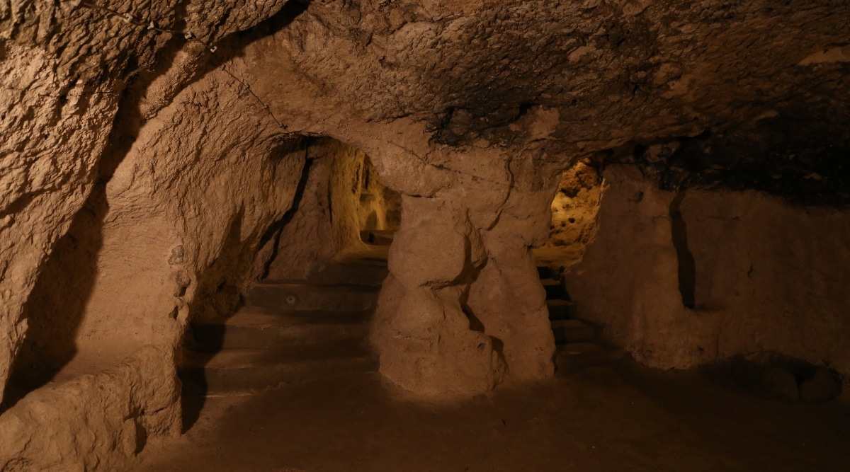 A photograph depicting the interior of Bluff Dwellers Cave in Missouri. The image showcases the cave's geological formations, including stalactites and stalagmites, illuminated for visibility.