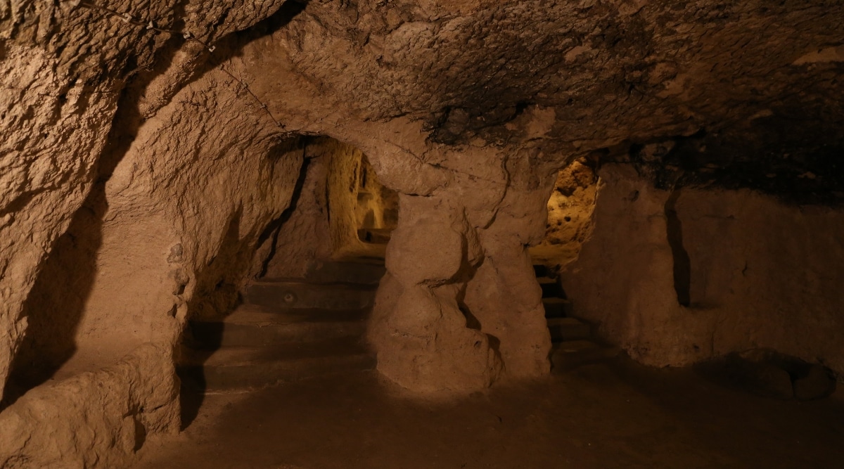 A photograph depicting the interior of Bluff Dwellers Cave in Missouri. The image showcases the cave's geological formations, including stalactites and stalagmites, illuminated for visibility.