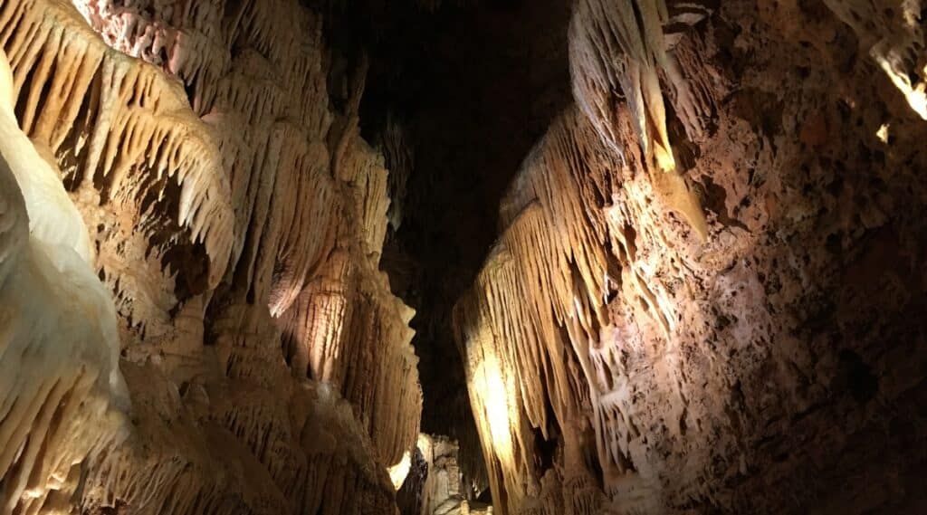 Bridal Cave in Missouri. Stalactites are growing across the top of the cave, with a long dark crevasse at the top in between the depths of the cave.
