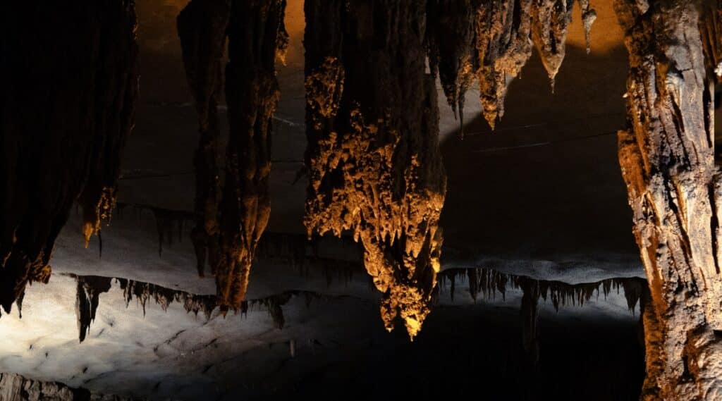 Fantastic caverns with stalactites growing downwards from the ceilings of the caves. The lighting is shining upwards on the rock formation, causing a yellowish looking rock formation.