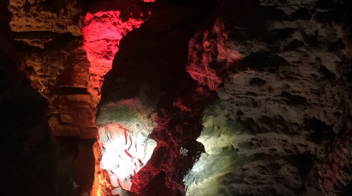 Red lights shining in stark caverns. The light shines upon the wall, which has many different rock formations growing in the background.