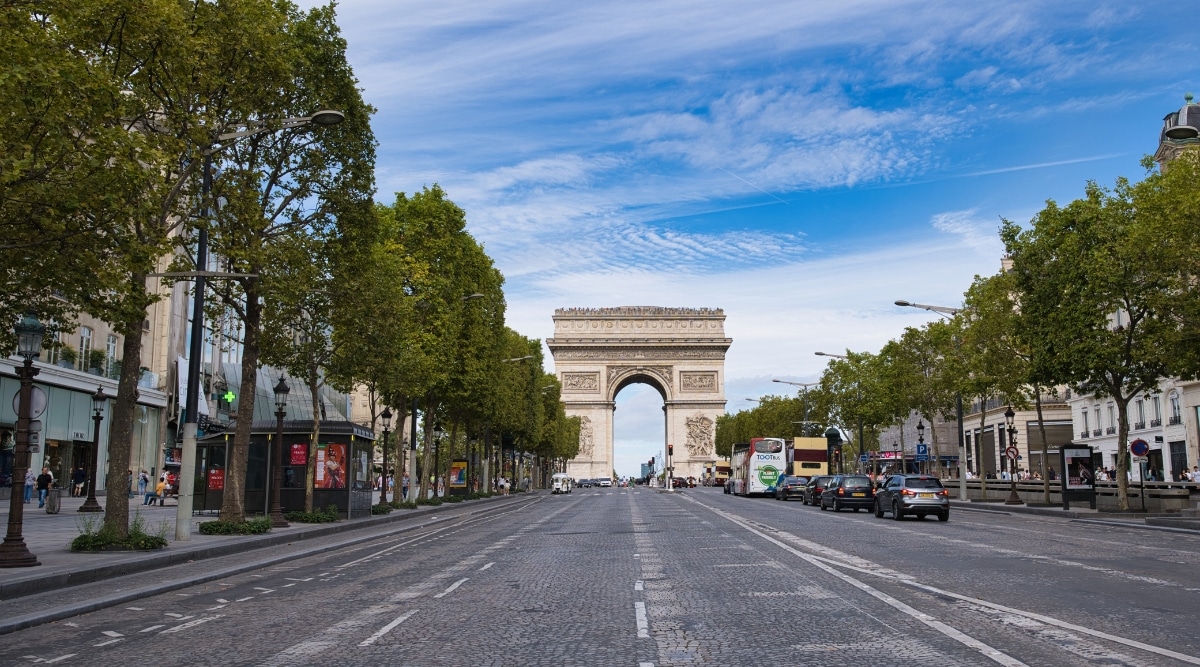 The Arc de Triomphe in Paris France, photographed from a distance down Champs-Elysees with cars driving and tourists walking.