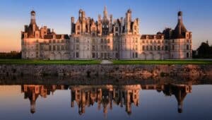 The famous Chateau de Chambord in Orleans, France, at sunset with the castle reflecting across the Loire River water.