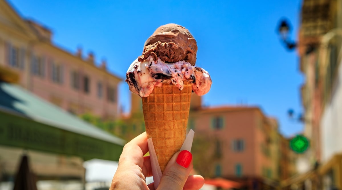 Close up image of a waffle cone with chocolate ice cream on top of cherry ice cream with a French city in the background.