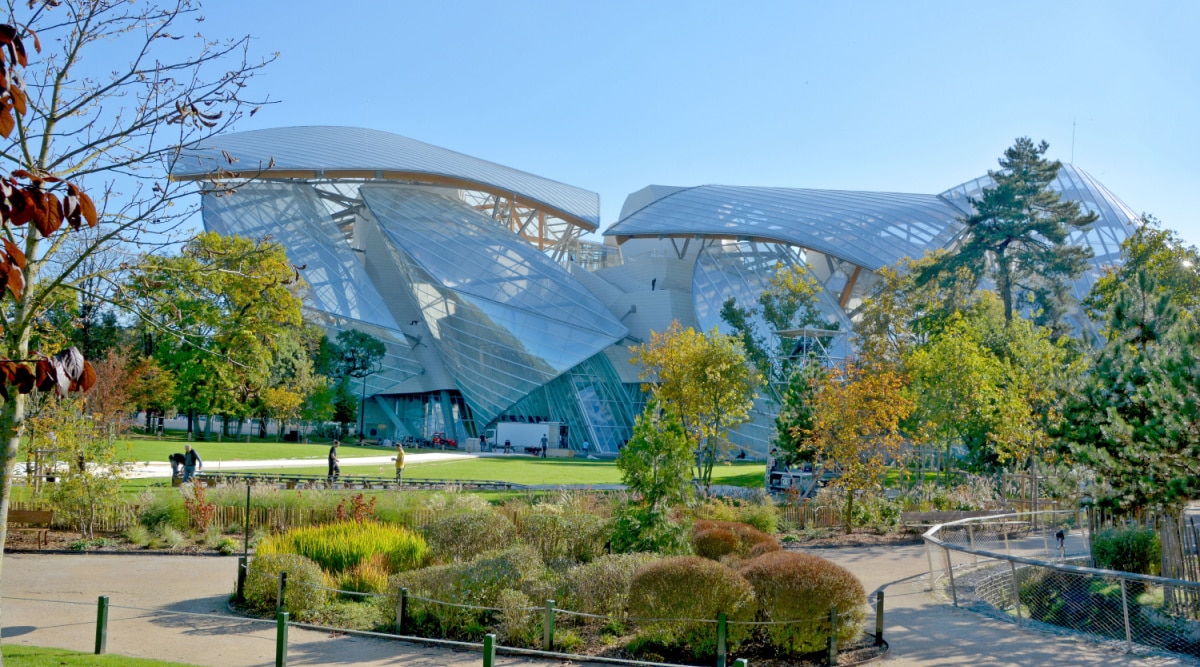 The exterior of the famous Louis Vuitton Foundation building surrounded by plants and grass on a clear sunny day in Paris, France.