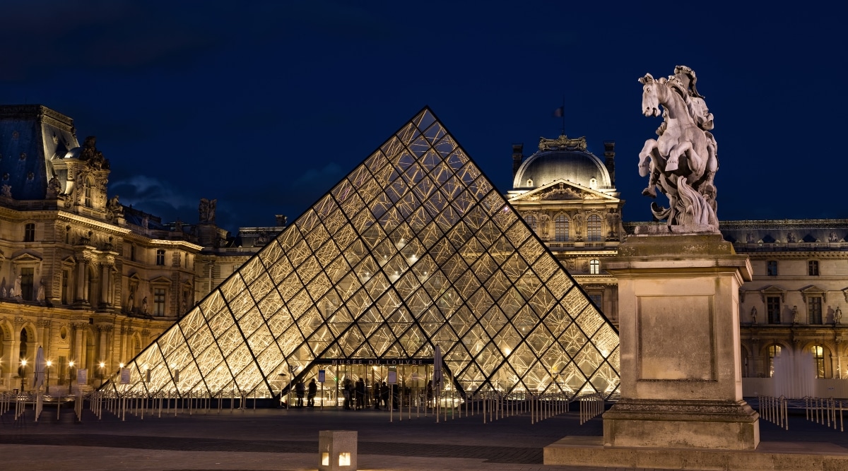 The Louvre museum in Paris France, photographed at night, illuminating the glass pyramid entrance.