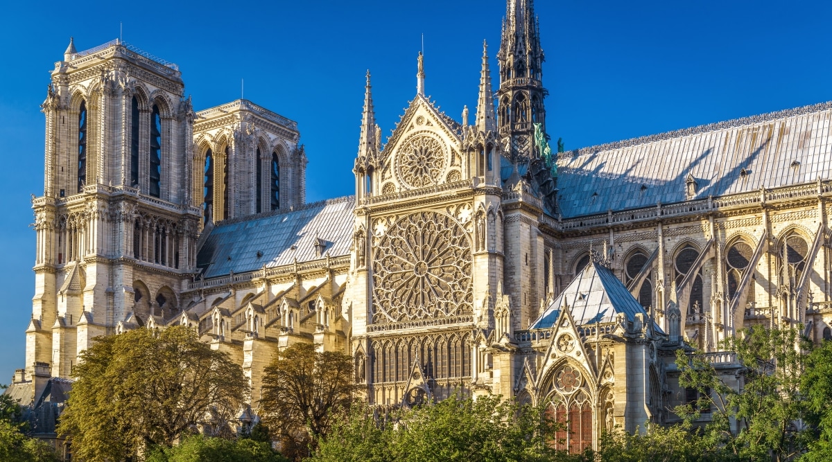 The Notre Dame Cathedral is a stunning example of French Gothic architecture, characterized by its towering spires, intricate stone carvings, and intricate stained glass windows. Notre Dame Cathedral is surrounded by various green trees.