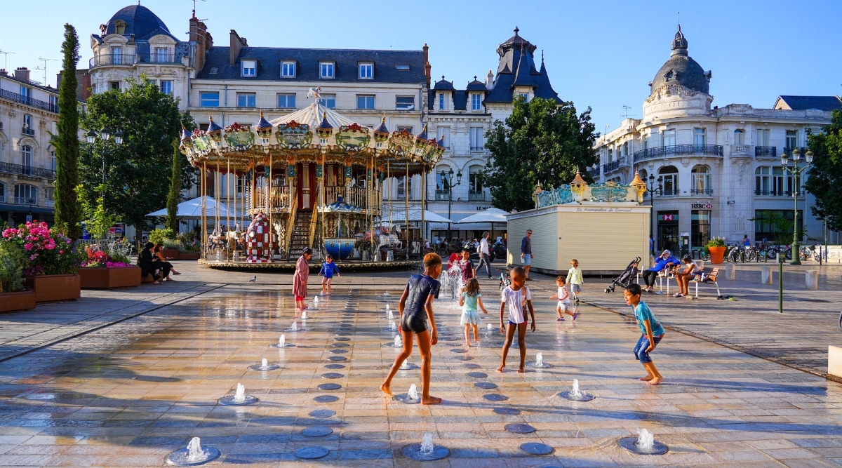 Children playing in the water fountains in the Place du Martroi on a sunny day in Orleans France. 