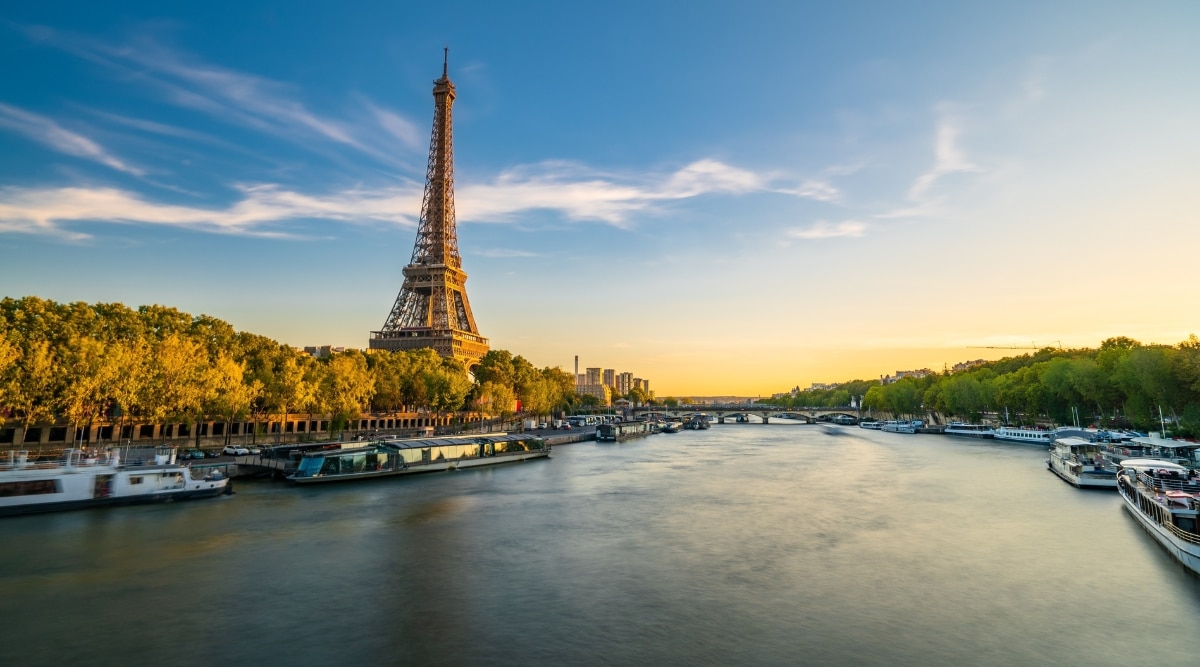 The River Seine flows through the Paris, dividing the city into its Left and Right Banks. The riverbanks are adorned with charming cafes, book stalls, and vibrant gardens. An Eiffel Tower can also be seen in the background.