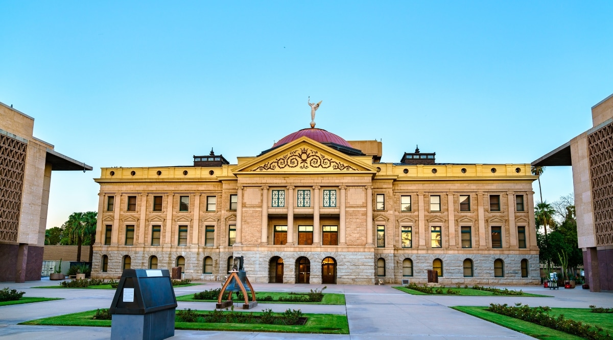 A photograph showcasing the Arizona Capitol Museum. The image features the elegant neoclassical façade of the museum, framed against a clear blue sky. The museum's architecture is characterized by grand columns, intricate detailing, and a copper dome.