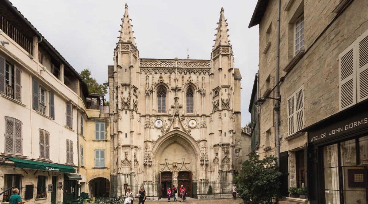 View of the Basilisque Saint-Pierre d'Avignon. The Basilique Saint-Pierre d'Avignon is a magnificent church in Avignon, France, known for its stunning Gothic architecture. The basilica stands tall with its intricate facade adorned with detailed carvings and statues. Tourists walk next to the church.
