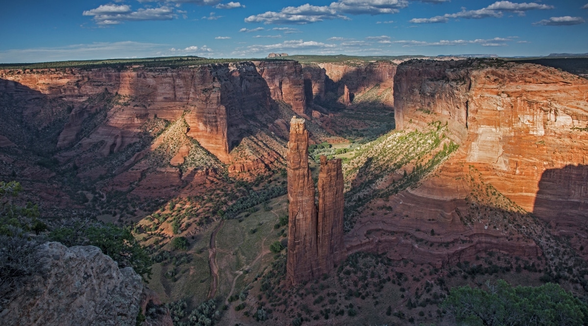 A captivating photo capturing the awe-inspiring beauty of Canyon de Chelly National Monument. The image showcases the deep sandstone canyons, with towering rock formations rising dramatically from the canyon floor. Towering red cliffs rise on either side, adding to the majestic scenery.