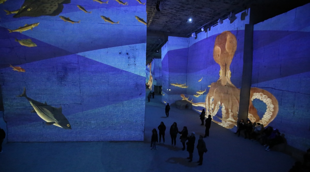 A mesmerizing visual of Carrieres des Lumieres. The image reveals vibrant and dynamic projections of famous artworks on the immense limestone walls of the former quarry, creating a captivating visual spectacle.