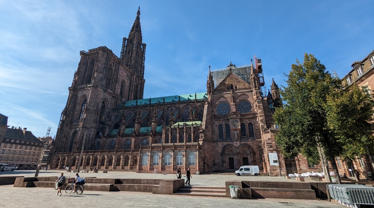 The Cathedrale Notre Dame de Strasbourg photographed from the street with a few tourists walking through on a clear sunny day in Strasbourg France.