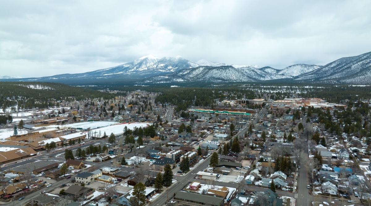 This captivating image presents an expansive view of the city of Flagstaff. The city is surrounded by the natural beauty of the region, with the San Francisco Peaks, including the snow-capped Humphreys Peak, forming a majestic backdrop. In the foreground, the city's streets and neighborhoods are visible, with a mix of architectural styles, from historic buildings to contemporary structures.