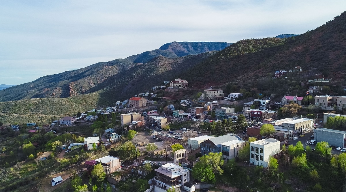 This image presents a captivating view of Jerome Ghost Town. The town is nestled on the side of a steep hill. An aerial view of the city reveals a mix of well-preserved historic buildings and contemporary modern houses scattered haphazardly across the hillside.