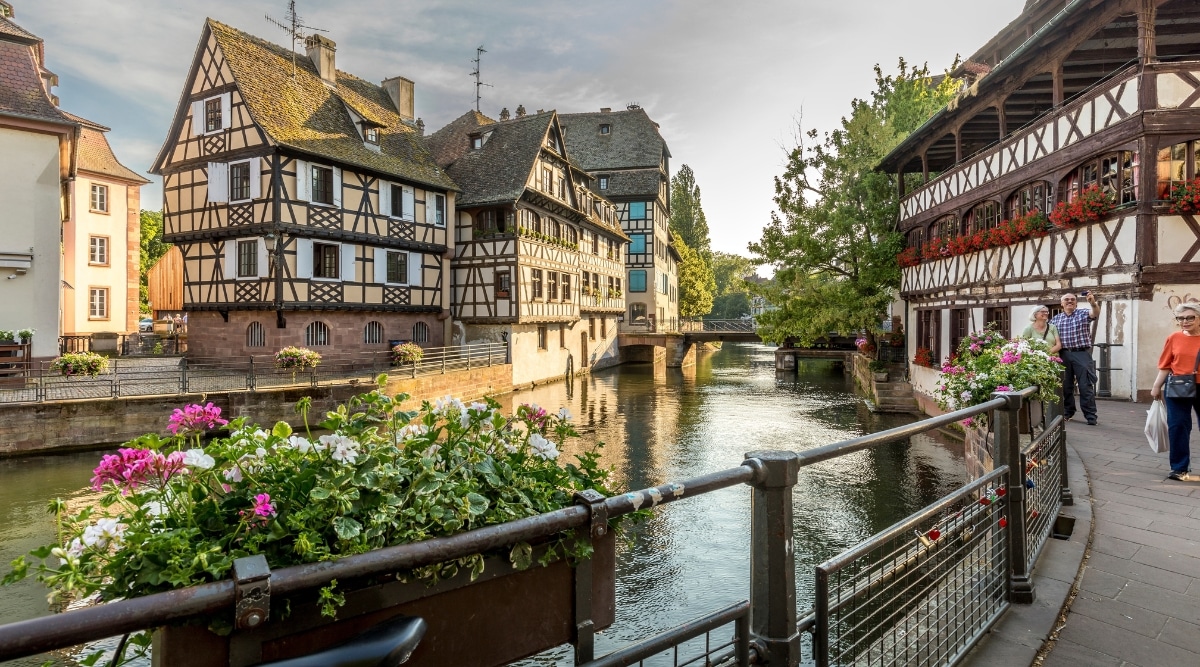 A view of the Ill River in Strasnbourg, France, with tourists walking admiring the old style architecture.