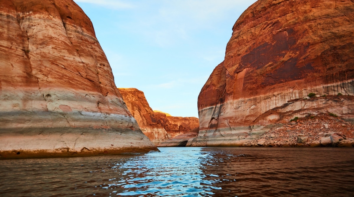 An enchanting image captures the serene beauty of Lake Powell, a man-made reservoir nestled within the dramatic red rock canyons of the American Southwest. The vast, shimmering lake stretches far into the distance, reflecting the clear, azure sky and the surrounding sandstone cliffs. 