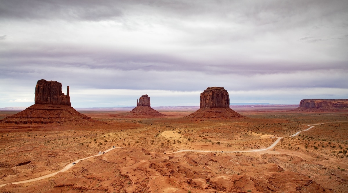View of Monument Valley Navajo Tribal Park. Monument Valley Navajo Tribal Park is an iconic, cinematic tableau, featuring towering sandstone buttes that rise dramatically from the desert floor. The red rock formations, with their smooth, majestic silhouettes, are set against a vast expanse of cloudy skies.
