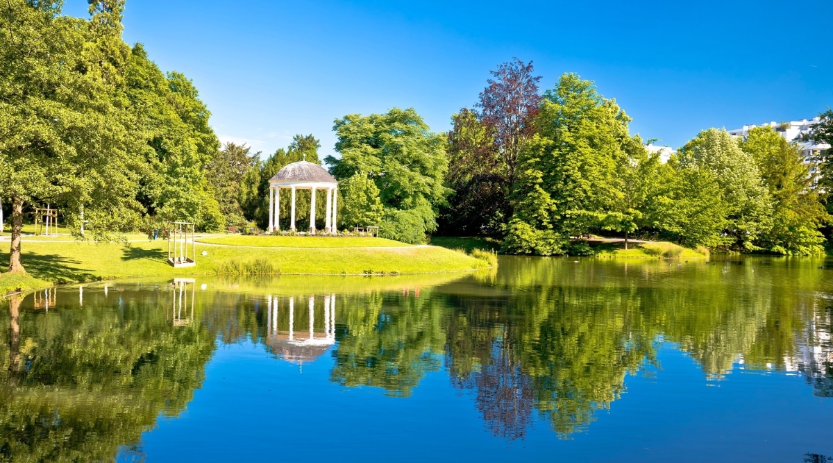 Parc de l’Orangerie in Strasbourg, France, a gazebo sits across a lake, reflecting in the water on a clear sunny summer day.