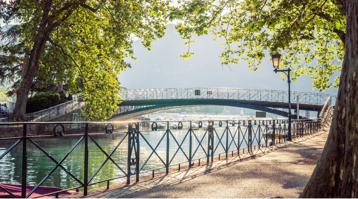 View of the Pont des Amours bridge on a bright day. The Pont des Amours, or "Bridge of Love," is a charming pedestrian bridge that spans the peaceful Canal du Vassé in Annecy. With its distinctive wrought-iron railings, delicate street lamps, and romantic arches, it exudes an air of timeless elegance.