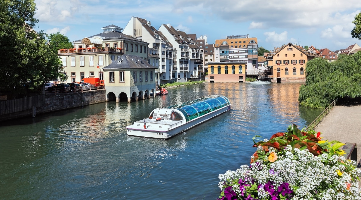 A cruise ship filled with tourists touring the Ill River in Strasbourg, France, on a sunny day.