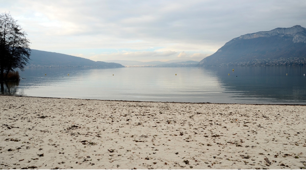 View of Saint-Jorioz Beach. Saint-Jorioz Beach is located on the shores of Lake Annecy. Its golden sand is framed by the emerald waters of the lake and a backdrop of verdant trees and mountains.