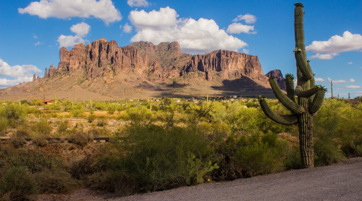 A mesmerizing view of the Superstition Mountains in Arizona. The image showcases the rugged terrain, towering peaks, and unique rock formations of this iconic mountain range. A field of lush green plants and cacti stretches out in front of the mountains.