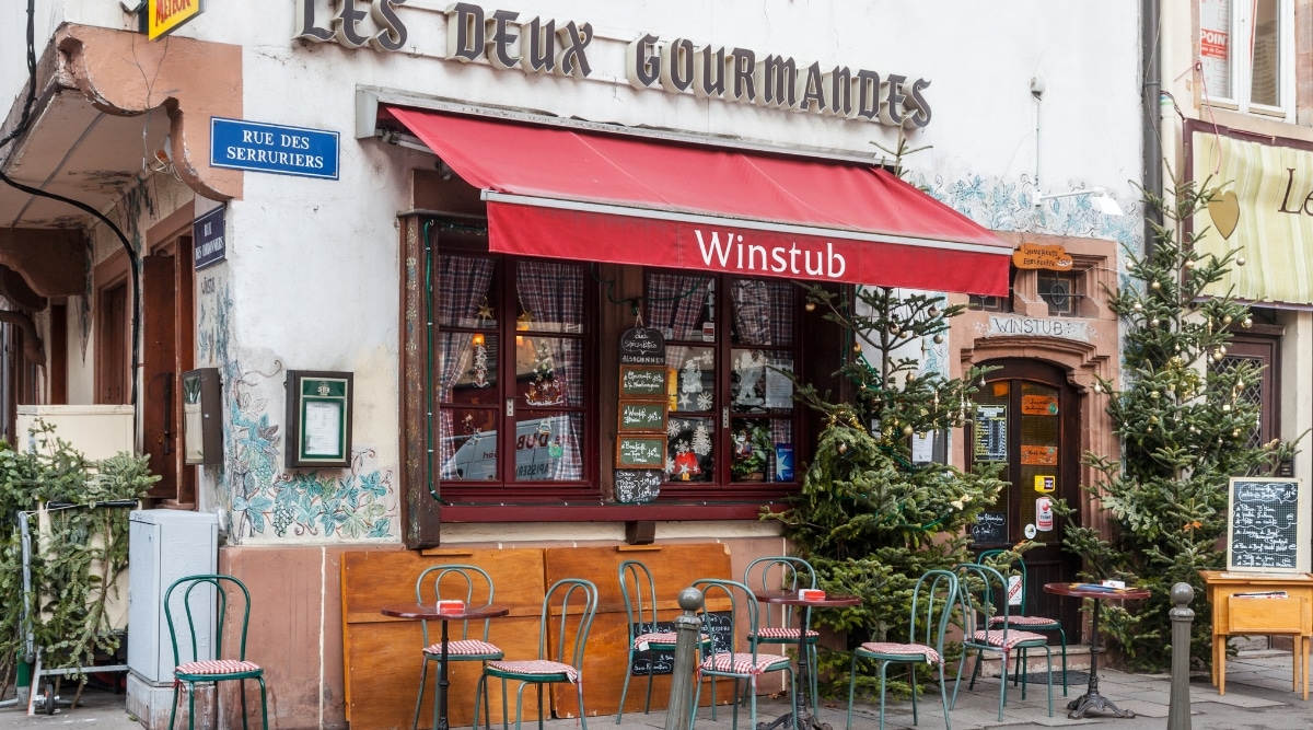 Les Deux Gourmandes, a local Strasbourg eatery referred to as a Winstub, in Strasbourg France. Empty chairs and tables sit outside the establishment. 