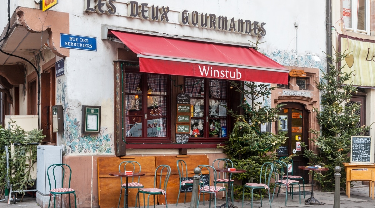 Les Deux Gourmandes, a local Strasbourg eatery referred to as a Winstub, in Strasbourg France. Empty chairs and tables sit outside the establishment.