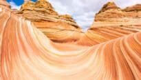 An image showcases the majestic Vermilion Cliffs. The cliffs rise majestically, their immense red, orange, and white sedimentary rock layers creating a vivid and awe-inspiring landscape. These layers, shaped by millennia of natural forces, exhibit intricate patterns and rich textures.
