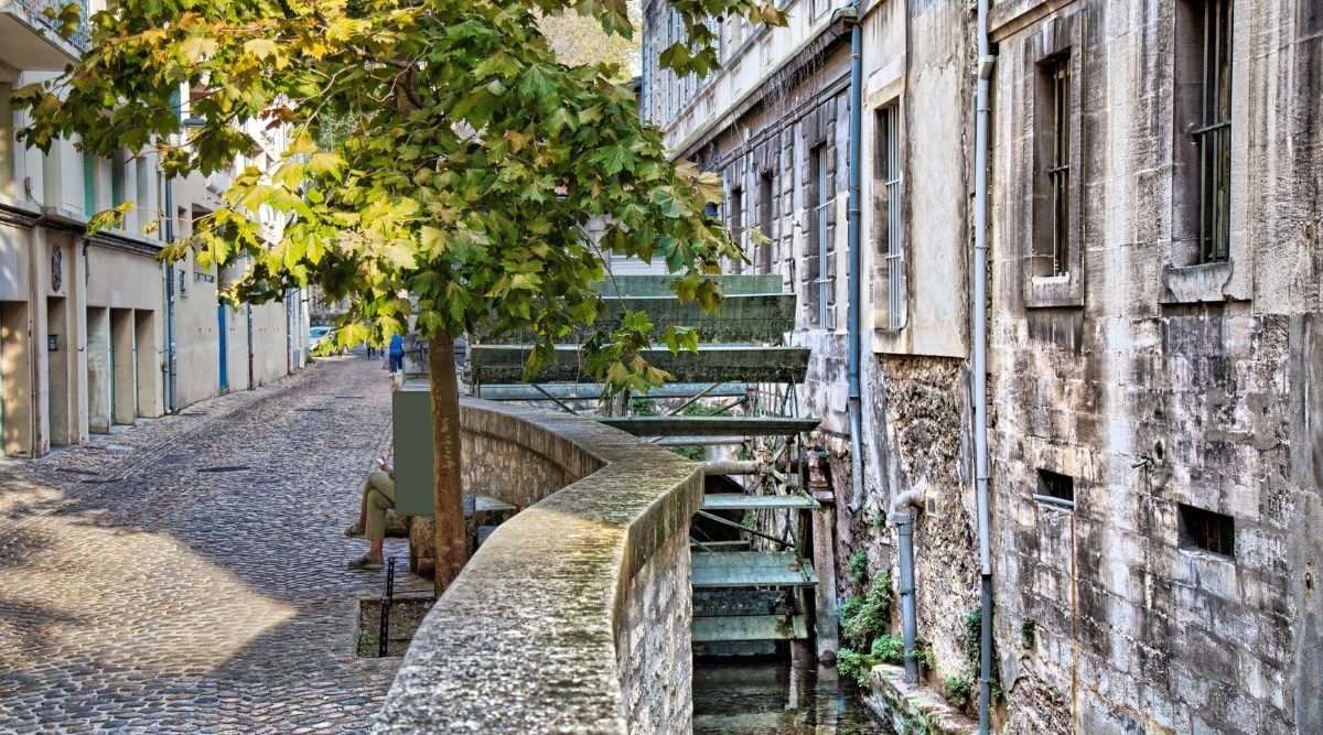 View of Rue des Teinturiers. Rue des Teinturiers is a picturesque and historic street located in the Avignon, France. This charming cobblestone thoroughfare is known for its vibrant character and the delightful network of small canals that run alongside it. The street is lined with beautifully preserved medieval buildings.