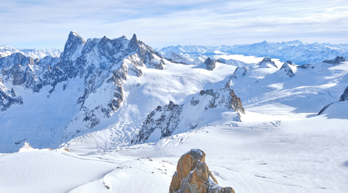 Aiguille du Midi in Chamonix, France. This iconic mountain peak, part of the Mont Blanc massif, stands tall against the azure sky, its majestic summit reaching dizzying heights. The jagged peaks of neighboring mountains surround Aiguille du Midi, creating a dramatic alpine panorama.