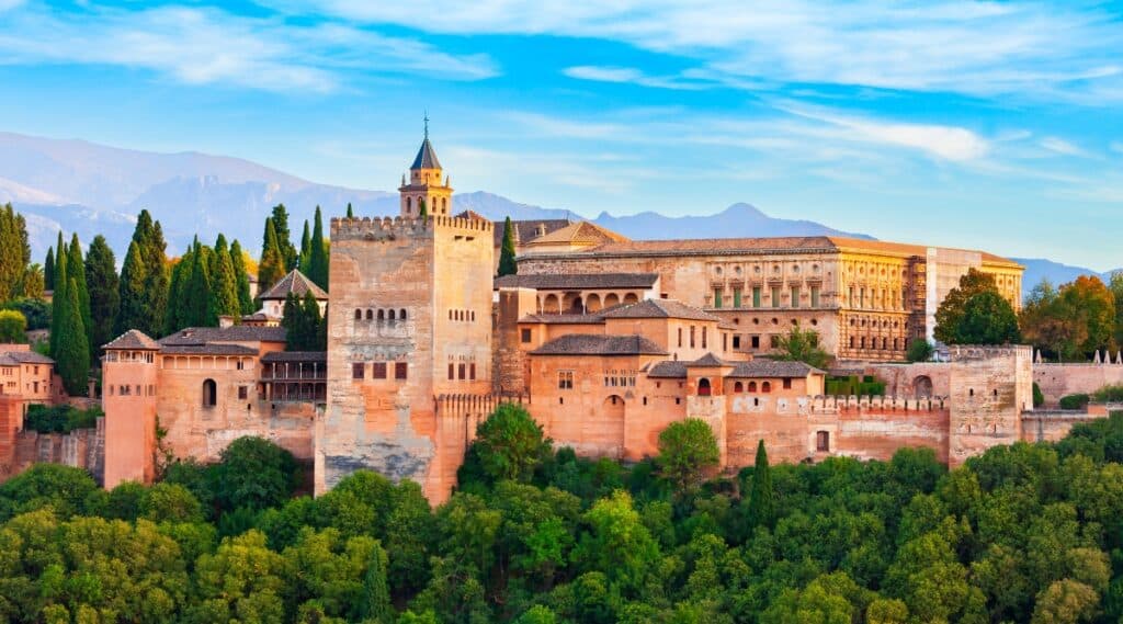 Alhambra, an iconic palace and fortress complex nestled against the backdrop of the Sierra Nevada mountains in Granada, Spain. The image captures the intricate details of the Moorish architecture, with ornate arches, delicate carvings, and expansive courtyards.