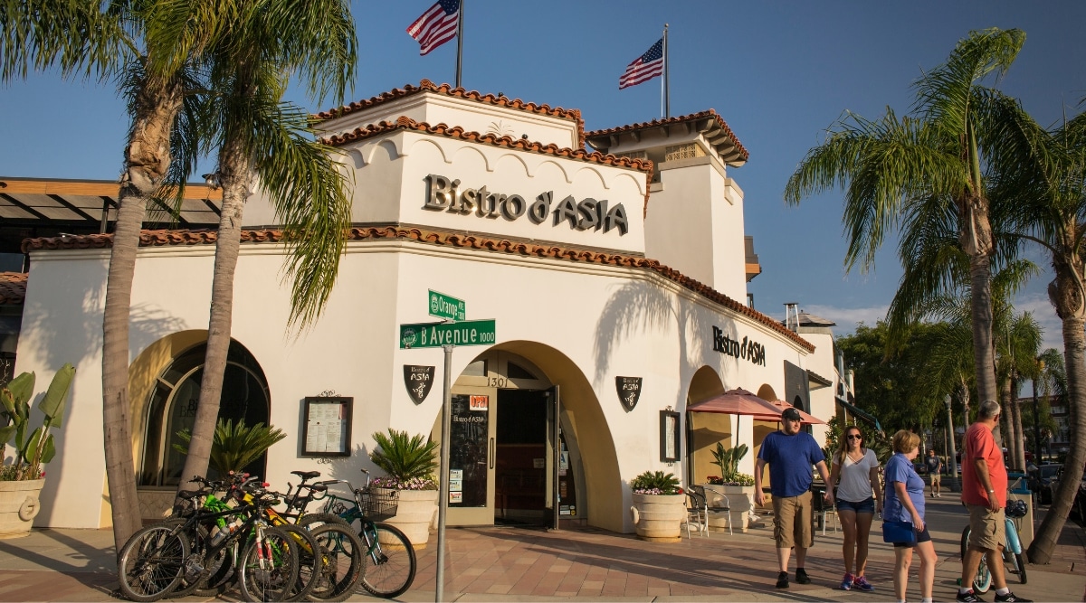 Entrance to Bistro d'Asia on the corner of Orange and B Avenue in Coronado, California, with bicycles parked and tourists walking along the sidewalk.