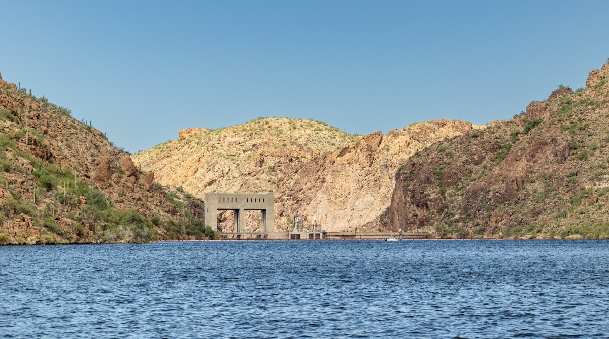 A photograph depicting Canyon Lake in Arizona. The image portrays the lake's waters surrounded by desert scenery. The shoreline is characterized by sparse vegetation, consistent with the arid environment. 