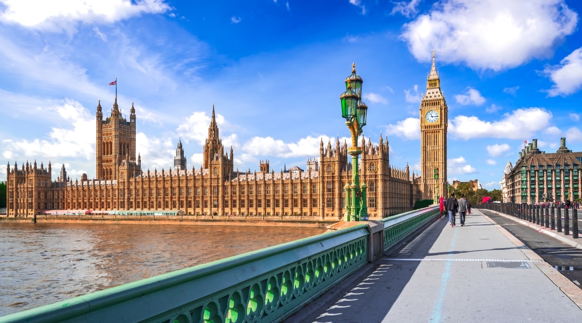 Houses of Parliament along the River Thames in London. The image showcases the historic architecture of the parliamentary buildings, with the iconic Big Ben clock tower standing tall against the city skyline. The intricate Gothic details of the façade and the ornate design elements.