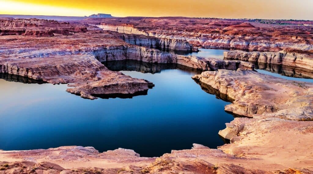 Lake Powell in Arizona. The image showcases the expansive reservoir surrounded by towering red rock formations and desert landscapes. The pristine blue waters of Lake Powell stretch into the distance, reflecting the clear sky above.