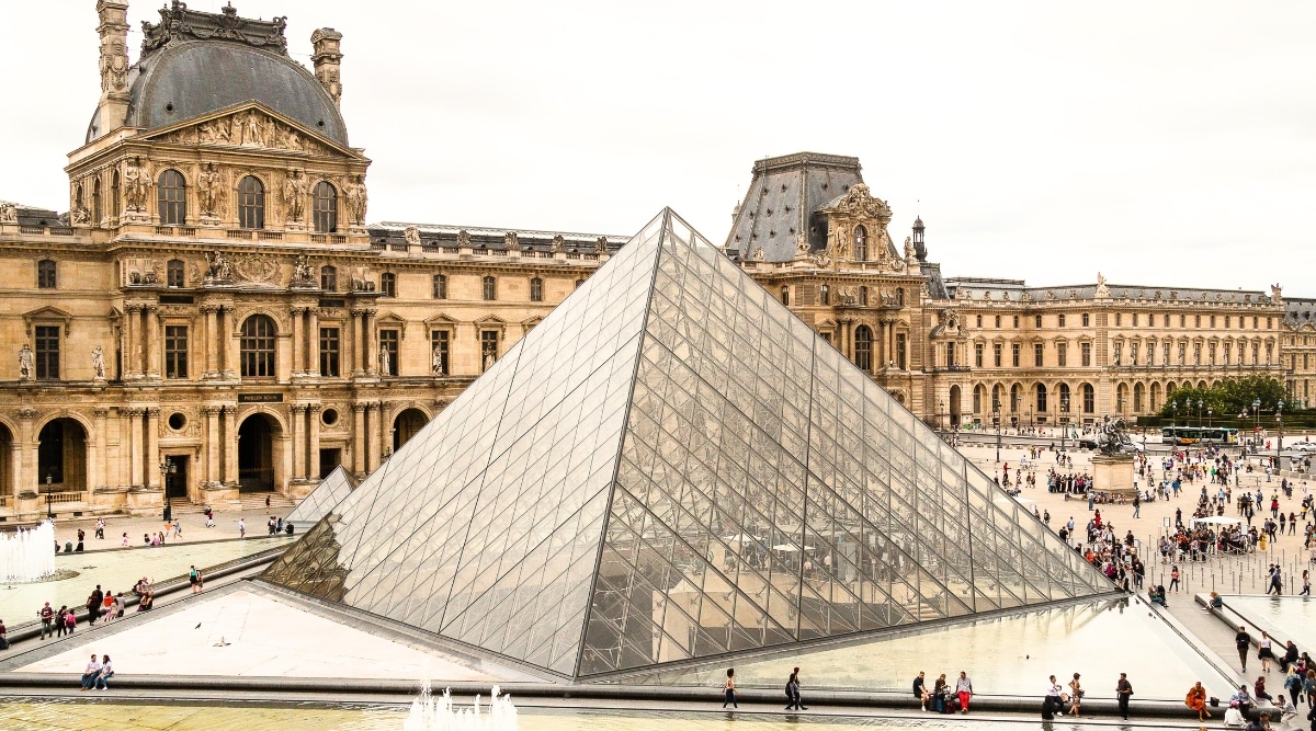 A striking photograph capturing the grandeur of the Louvre Museum, an iconic cultural landmark in Paris. The image showcases the museum's historic facade, adorned with ornate columns and archways. The Louvre's glass pyramid, a modern architectural marvel, adds a touch of contemporary elegance to the scene, juxtaposed against the classical backdrop. The expansive plaza in front of the museum bustles with activity, as tourists and art enthusiasts explore this cultural treasure trove.